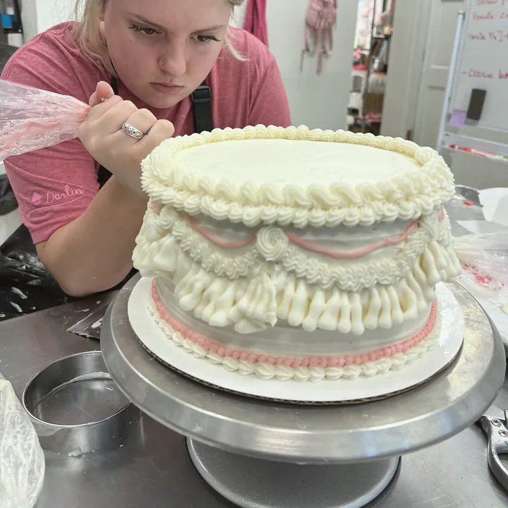 Piping buttercream ruffles onto a pink layer cake