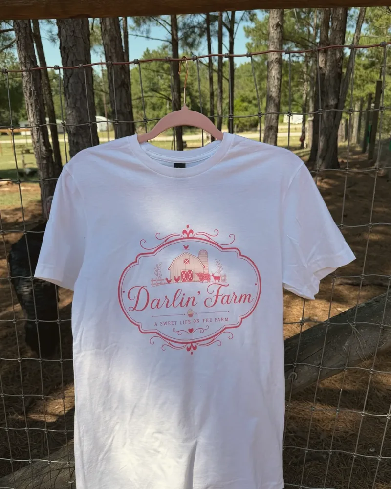 White Darlin' Farm shirt with the pink farm crest, hanging on the fence